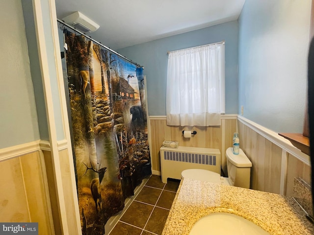 bathroom featuring vanity, tile patterned flooring, toilet, wooden walls, and radiator