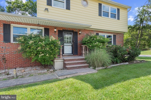 entrance to property featuring brick siding and a lawn