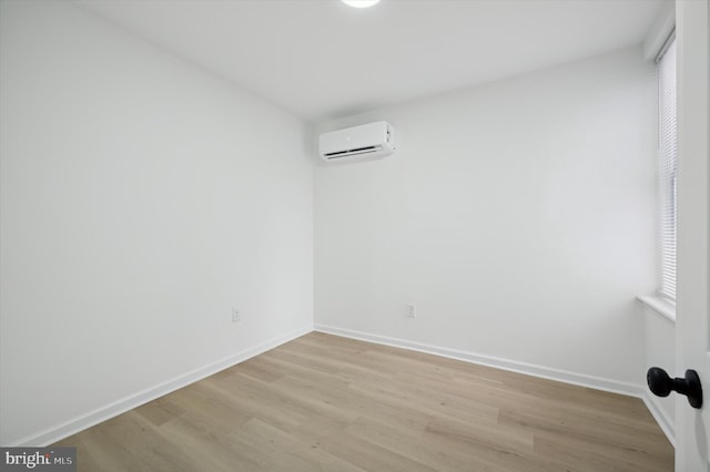 unfurnished room featuring an AC wall unit, light wood-type flooring, and baseboards