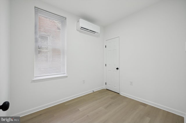 empty room with light wood-style floors, a wall unit AC, and baseboards