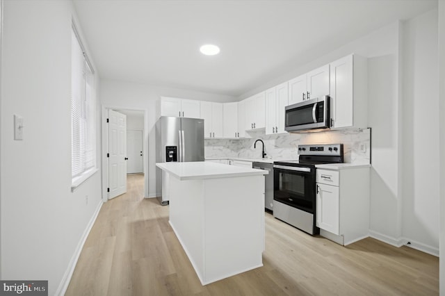 kitchen featuring decorative backsplash, appliances with stainless steel finishes, a center island, light countertops, and white cabinetry