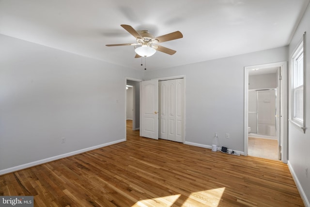 unfurnished bedroom featuring ceiling fan, ensuite bathroom, hardwood / wood-style floors, and a closet