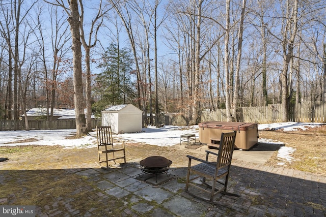 snow covered patio featuring an outdoor fire pit, a hot tub, and a storage unit