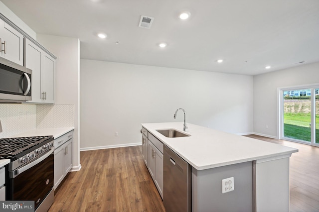 kitchen with appliances with stainless steel finishes, sink, backsplash, dark hardwood / wood-style flooring, and a center island with sink