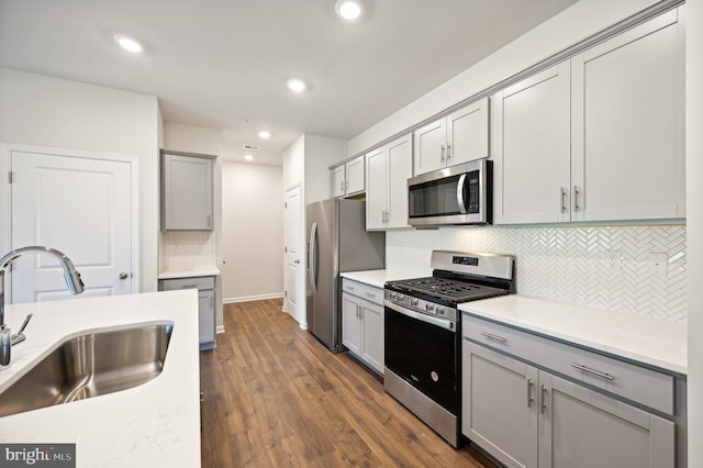 kitchen with sink, gray cabinets, appliances with stainless steel finishes, backsplash, and dark hardwood / wood-style flooring