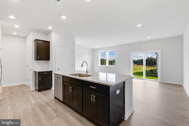 kitchen featuring an island with sink, sink, stainless steel dishwasher, light stone counters, and light wood-type flooring