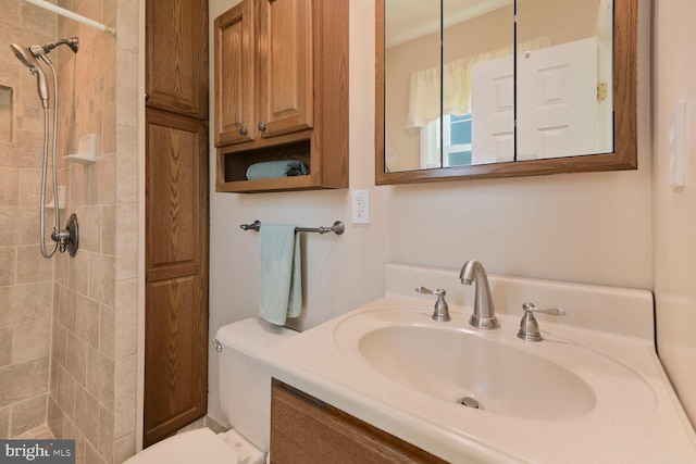 bathroom with toilet, vanity, and tiled shower