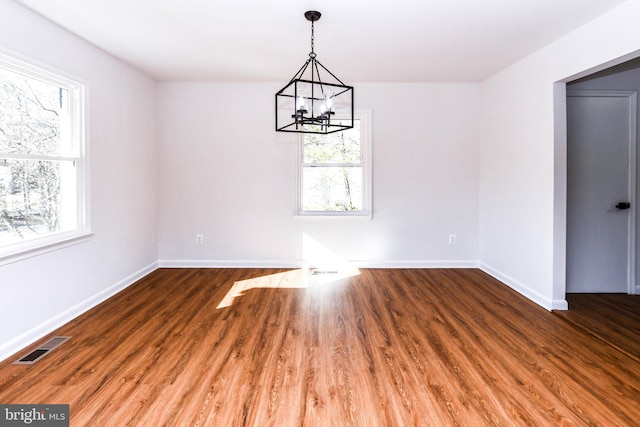 unfurnished dining area with dark wood-type flooring, a healthy amount of sunlight, and a chandelier