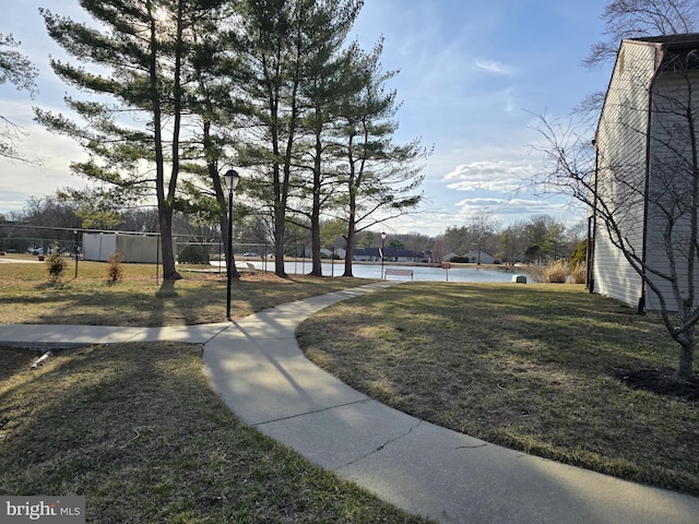 view of community featuring a yard, a water view, and fence