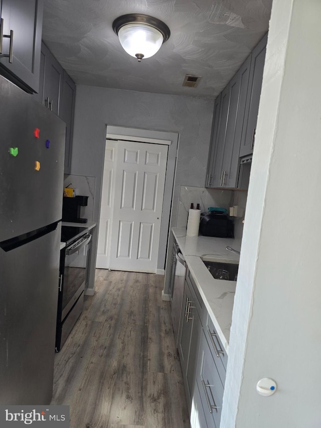 kitchen with wood finished floors, visible vents, appliances with stainless steel finishes, gray cabinets, and light stone countertops