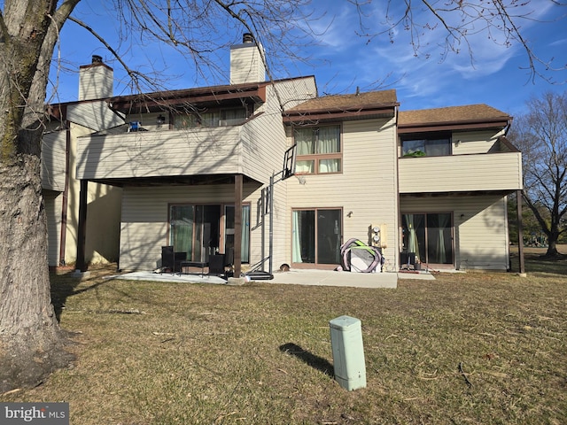 back of house with a balcony, a patio area, a chimney, and a yard