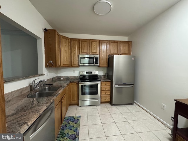 kitchen with sink, appliances with stainless steel finishes, dark stone counters, and light tile patterned flooring