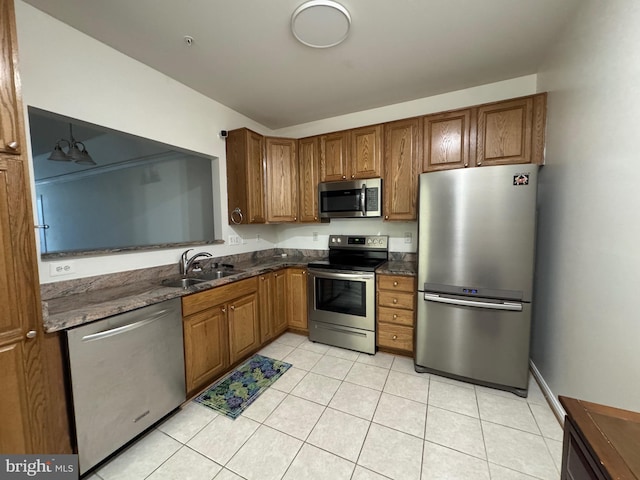 kitchen with dark stone countertops, light tile patterned floors, stainless steel appliances, and sink