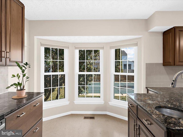 kitchen with dark stone countertops, a healthy amount of sunlight, baseboards, visible vents, and a sink