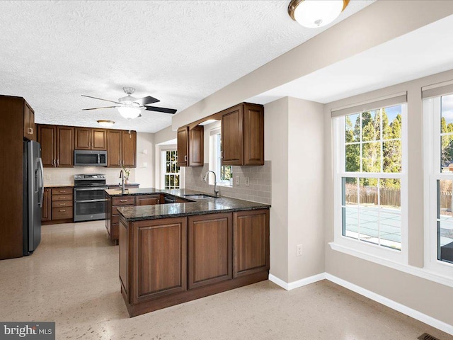 kitchen with a peninsula, a sink, decorative backsplash, stainless steel appliances, and light speckled floor