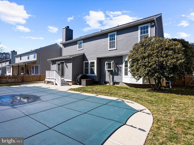 back of property with a chimney, a fenced in pool, fence, and a lawn