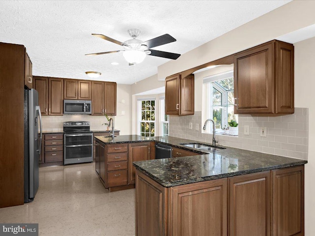 kitchen with decorative backsplash, dark stone countertops, a peninsula, stainless steel appliances, and a sink