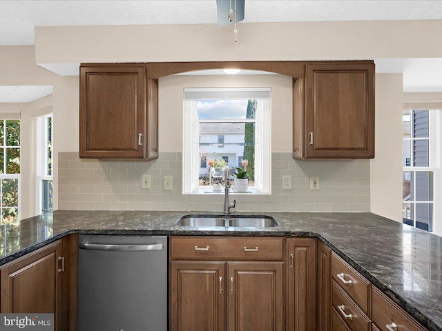 kitchen with a sink, tasteful backsplash, stainless steel dishwasher, dark stone counters, and a peninsula