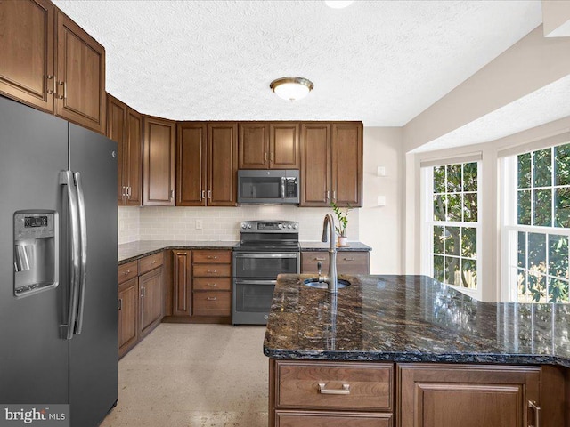 kitchen with a sink, backsplash, a textured ceiling, dark stone counters, and appliances with stainless steel finishes