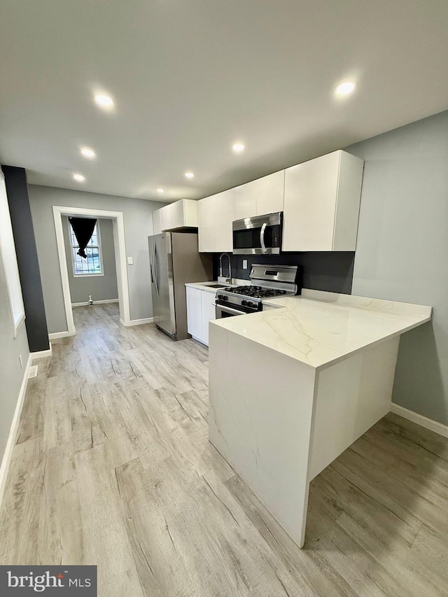 kitchen with light hardwood / wood-style flooring, stainless steel appliances, light stone countertops, white cabinetry, and kitchen peninsula