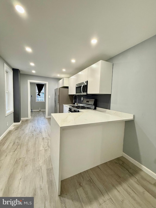 kitchen featuring stainless steel appliances, white cabinetry, kitchen peninsula, and light stone counters