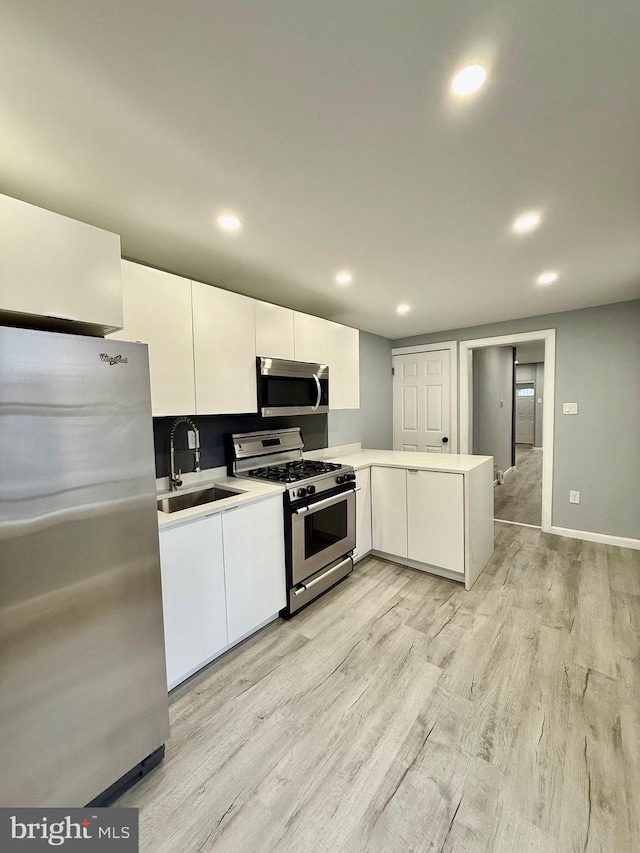 kitchen with appliances with stainless steel finishes, light hardwood / wood-style flooring, sink, and white cabinetry