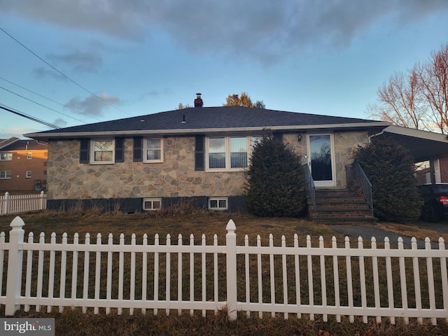 view of front of house with entry steps, stone siding, a fenced front yard, and roof with shingles