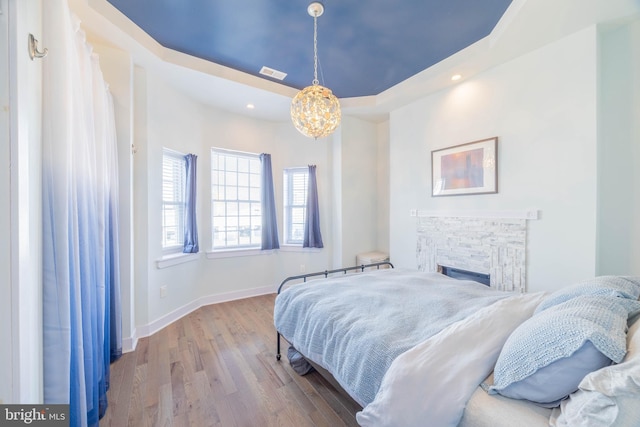 bedroom with a fireplace, a raised ceiling, visible vents, wood finished floors, and baseboards