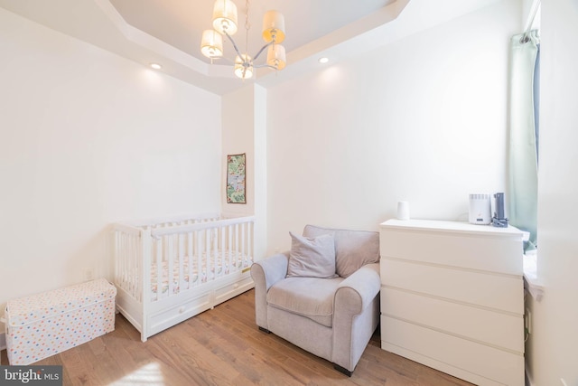 bedroom with a chandelier, a raised ceiling, and wood finished floors