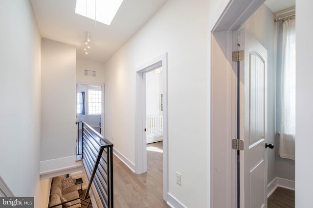 hall featuring light wood-style flooring, a skylight, visible vents, an upstairs landing, and baseboards