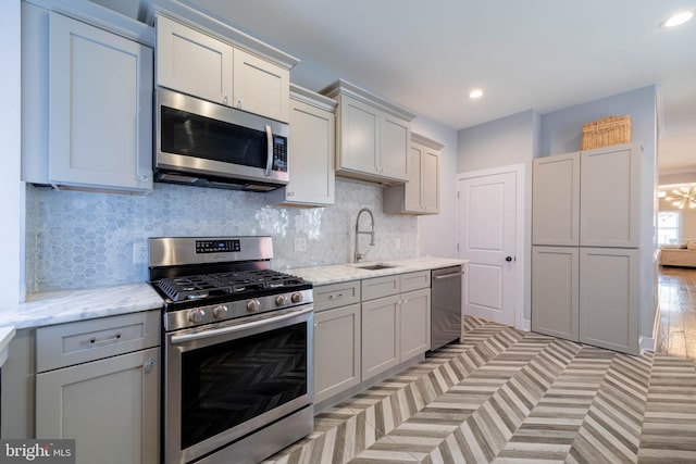 kitchen with light stone counters, stainless steel appliances, recessed lighting, backsplash, and a sink