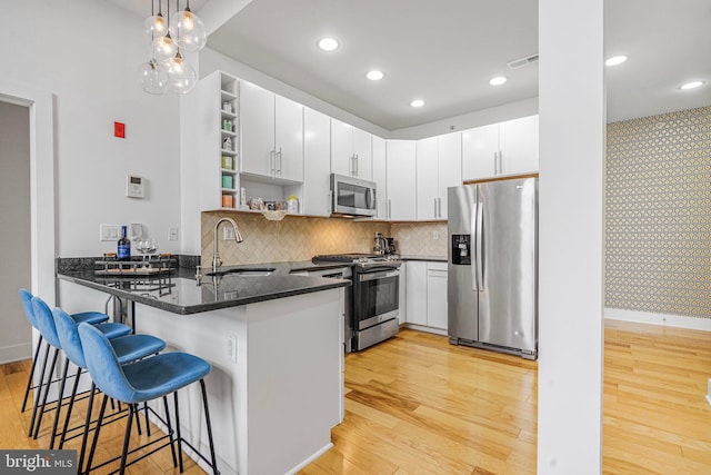 kitchen with stainless steel appliances, a peninsula, a sink, light wood-style floors, and open shelves