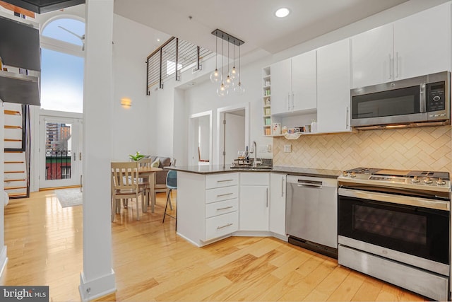 kitchen featuring stainless steel appliances, white cabinetry, open shelves, light wood finished floors, and dark countertops