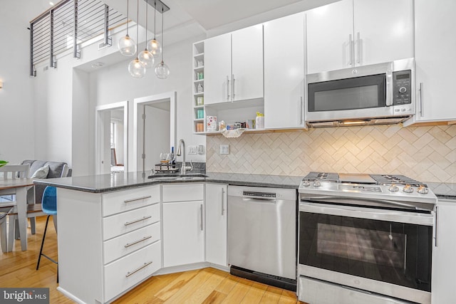 kitchen featuring open shelves, stainless steel appliances, light wood-style flooring, a sink, and a peninsula