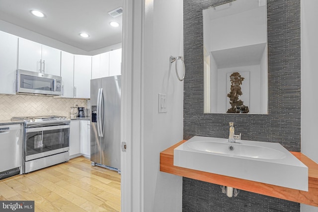 kitchen featuring stainless steel appliances, visible vents, white cabinetry, light wood finished floors, and tasteful backsplash