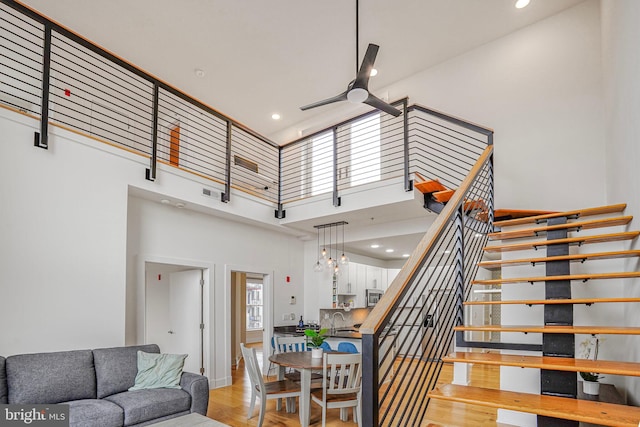 stairs featuring ceiling fan, a high ceiling, wood finished floors, and recessed lighting