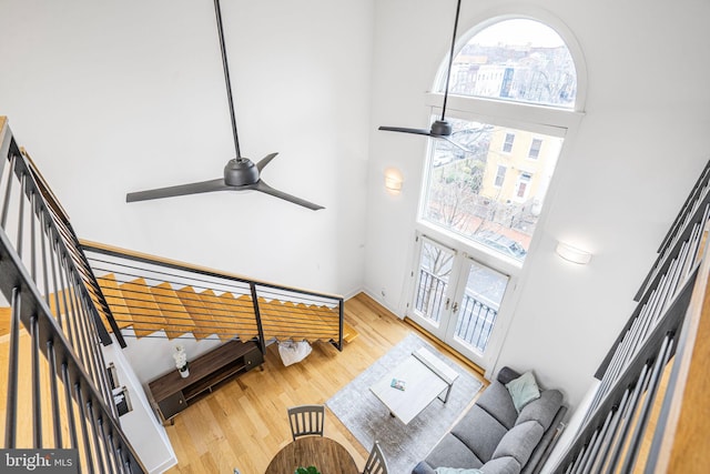 living area featuring a towering ceiling, ceiling fan, stairway, wood finished floors, and french doors