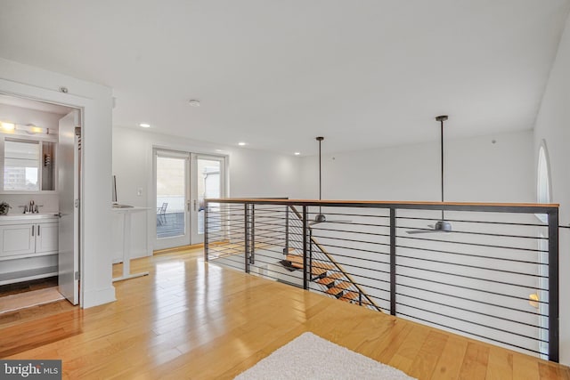 corridor with french doors, light wood finished floors, recessed lighting, a sink, and an upstairs landing