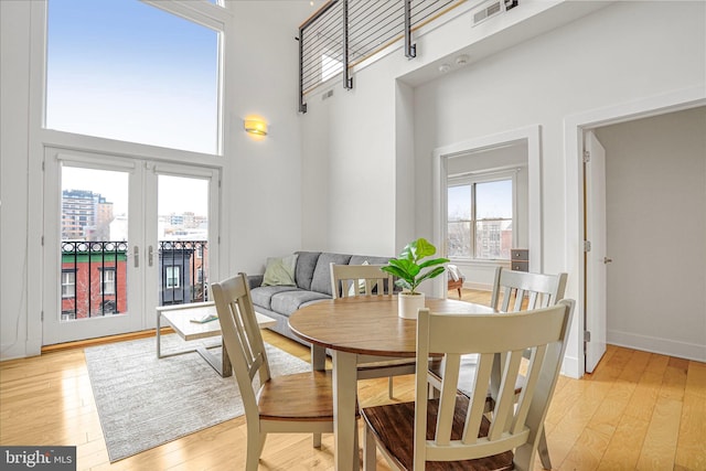 dining space with french doors, light wood finished floors, a towering ceiling, and visible vents