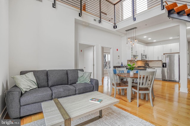 living area featuring a chandelier, a high ceiling, recessed lighting, and light wood-style floors