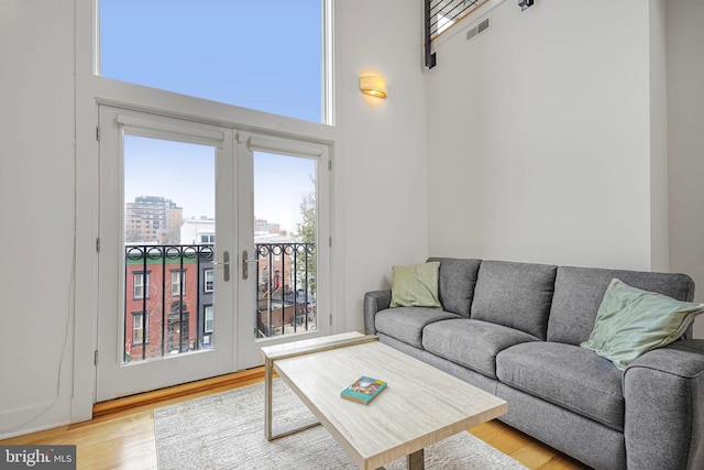 living area with visible vents, a towering ceiling, wood finished floors, a city view, and french doors