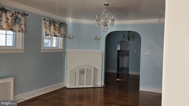 unfurnished dining area with arched walkways, radiator, an inviting chandelier, dark wood-type flooring, and baseboards