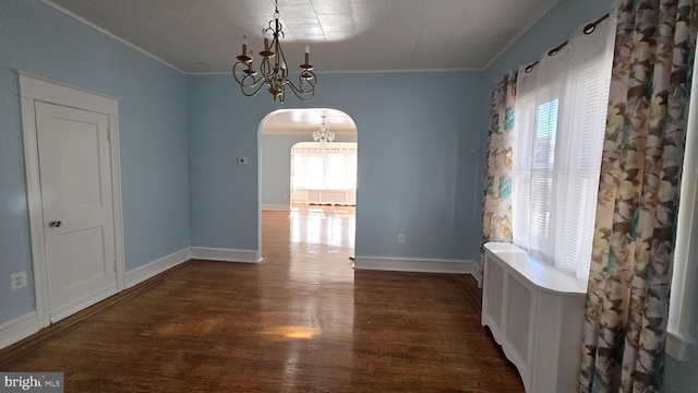 unfurnished dining area with arched walkways, crown molding, an inviting chandelier, dark wood-type flooring, and baseboards