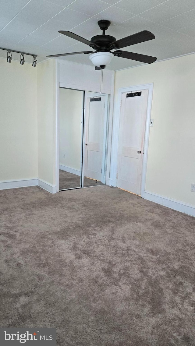 unfurnished bedroom with carpet floors, track lighting, baseboards, and a closet