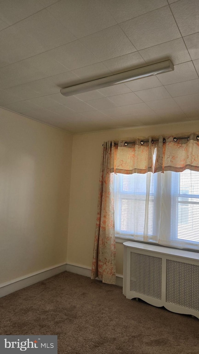 empty room featuring baseboards, carpet flooring, and radiator