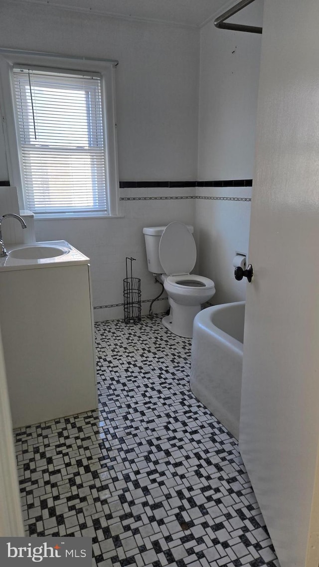 bathroom with wainscoting, vanity, toilet, and tile walls