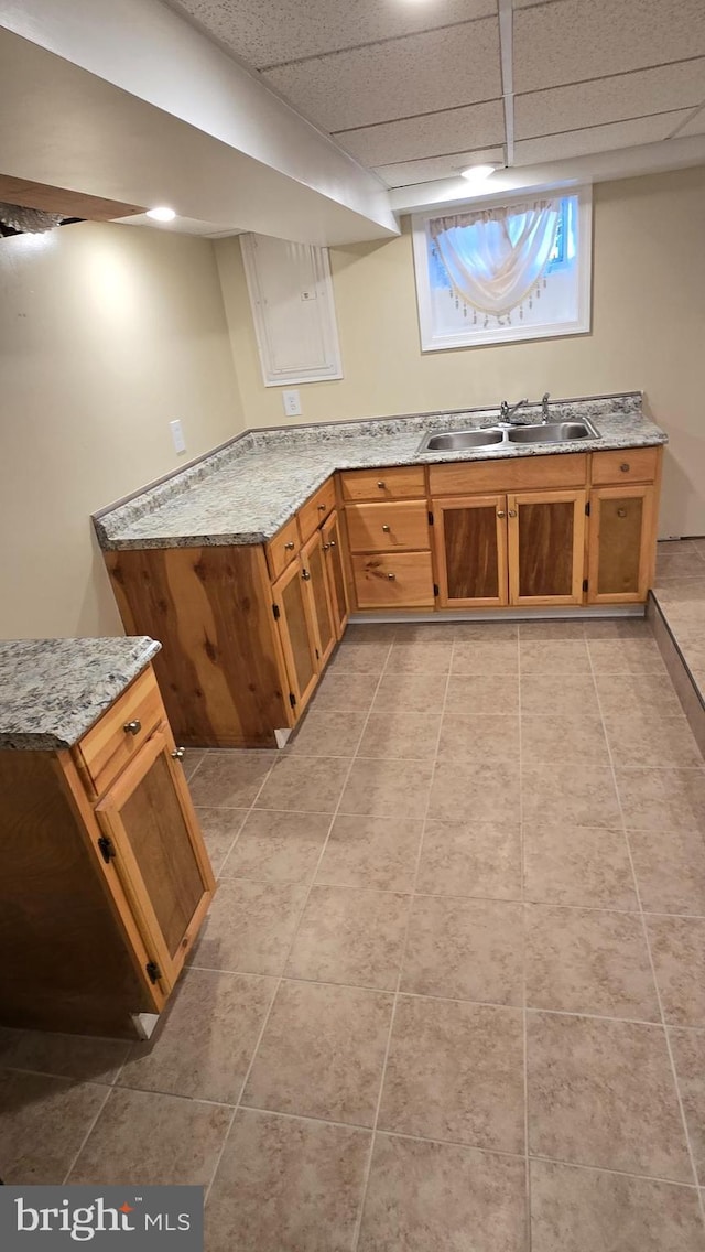 kitchen featuring light stone counters, light tile patterned flooring, a drop ceiling, a sink, and brown cabinets