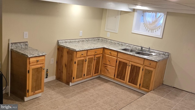 kitchen with light stone counters, brown cabinets, a sink, and light tile patterned floors