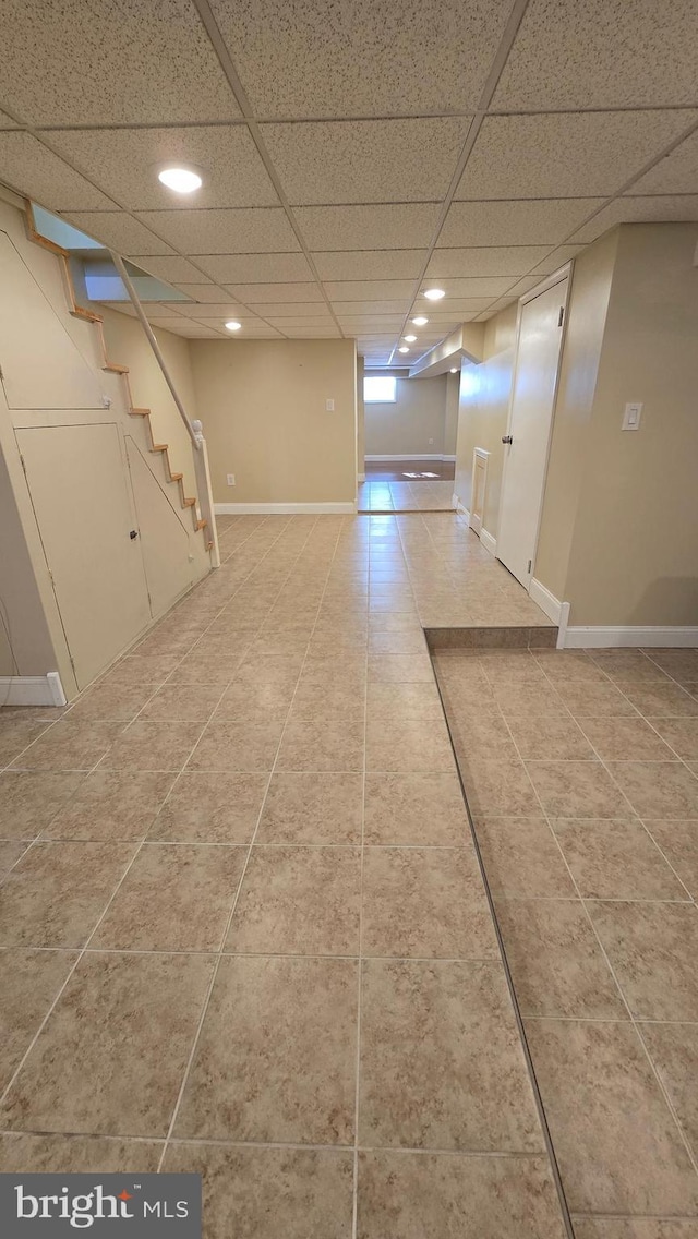 below grade area featuring stairs, a drop ceiling, baseboards, and tile patterned floors