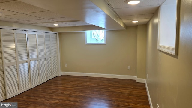 below grade area featuring dark wood-style floors, a drop ceiling, and baseboards